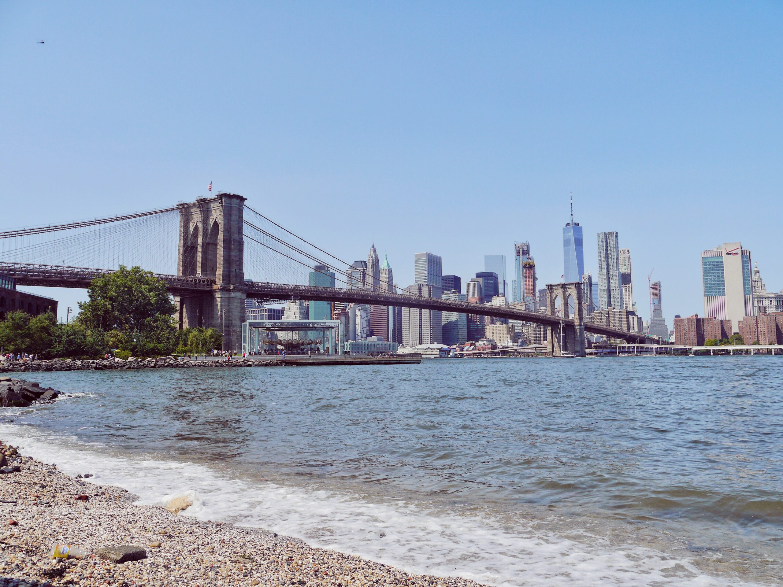 The Brooklyn Bridge from a pebble beach with the Manhattan skyline in the backdrop