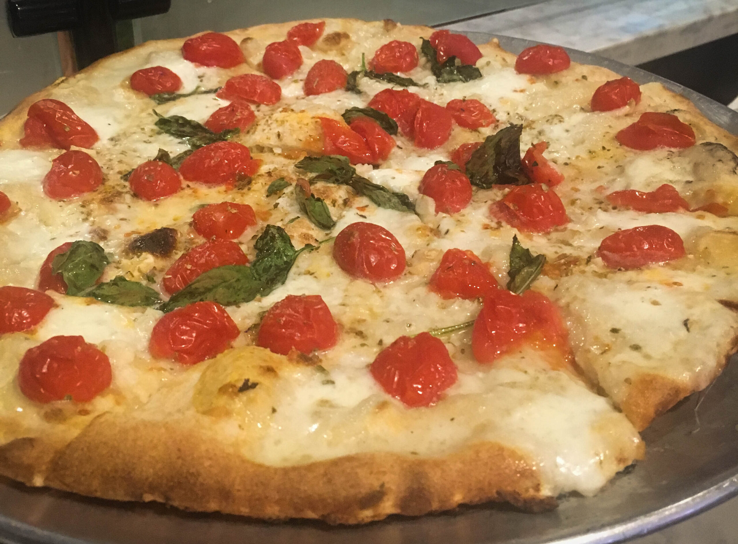 Whole pizza pie with cheese tomatoes and basil leaves