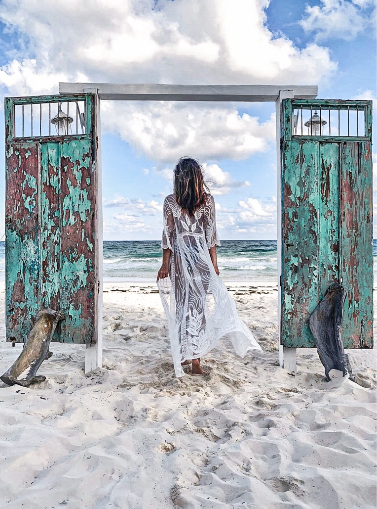 Girl in white beach cover-up walking through a set of frameless doors on the beach