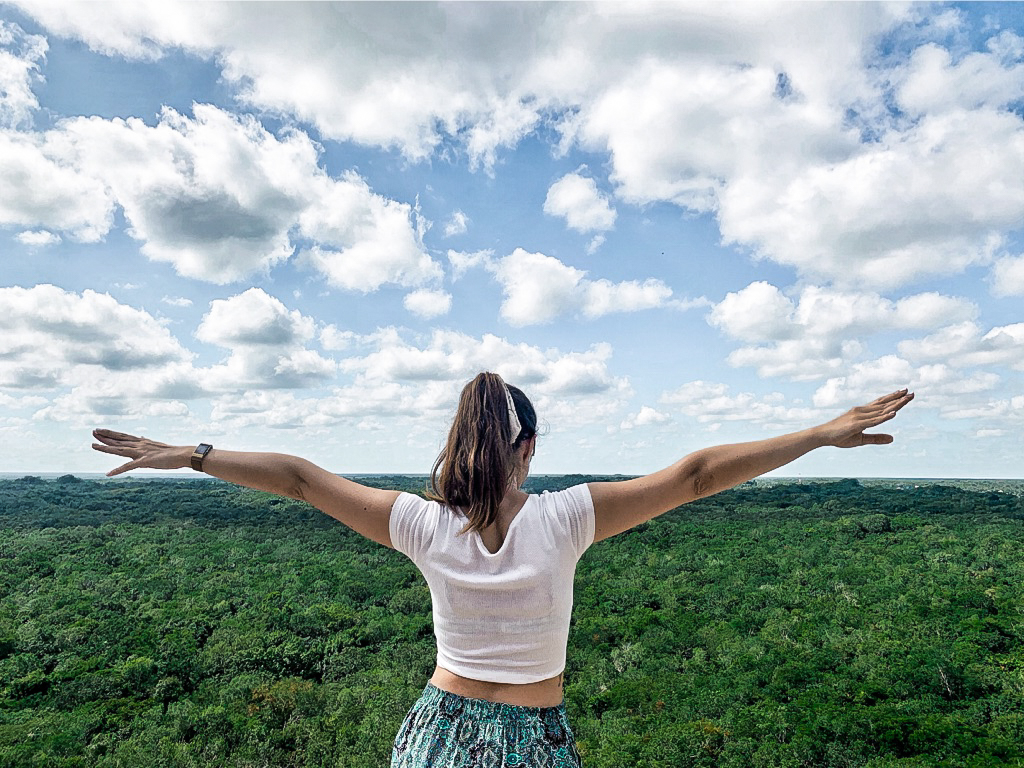 Girl spreading out arms against a backdrop of jungle and sky in Coba